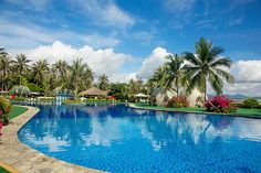 a large swimming pool surrounded by lush green trees and blue skies with clouds in the background