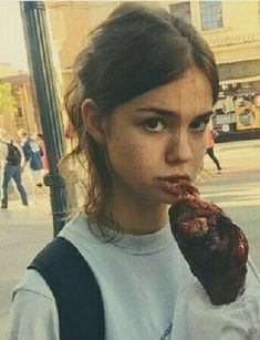 a young woman is eating something outside on the street