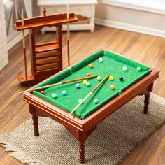 a miniature pool table with cues and balls on the floor next to a rocking chair