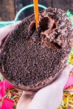 a person holding a chocolate frosted donut with a candle in it