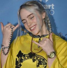 a woman with blonde hair wearing a yellow shirt and holding her hand up to the side