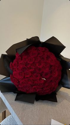 a large bouquet of red roses sitting on top of a black ribbon wrapped round object