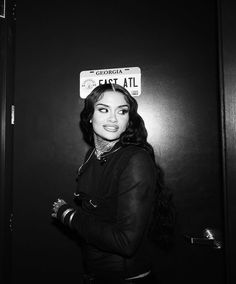 a black and white photo of a woman in front of a door with a sign on her head