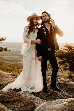 a man and woman standing on top of a rocky hill next to each other wearing cowboy hats