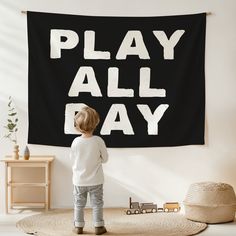 a little boy standing in front of a play all day wall hanging