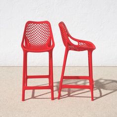 two red chairs sitting next to each other on top of a cement floor in front of a white wall