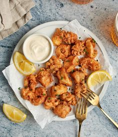 a white plate topped with fried shrimp next to lemon wedges and dipping sauce on a table