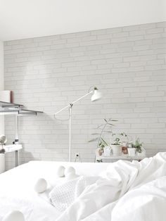 a bed with white sheets and pillows next to a lamp on a table in front of a brick wall