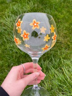 a hand holding a wine glass with flowers painted on it