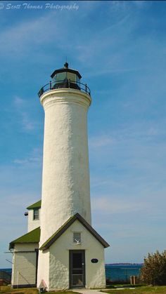 a white lighthouse sitting on top of a lush green field next to the ocean in front of a blue sky