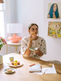 a woman sitting at a table eating food and drinking from a cup in front of her