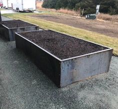 two large metal containers filled with dirt sitting on top of a gravel road