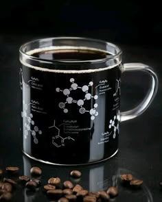 a black coffee mug filled with liquid surrounded by coffee beans and caffetti on a dark surface