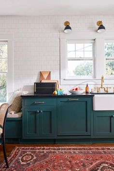 a kitchen with green cabinets and an area rug in front of the sink that has gold faucets on it