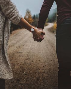 two people holding hands while walking down a dirt road