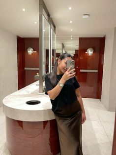 a woman taking a selfie in front of a bathroom mirror while wearing a skirt