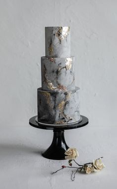 a three tiered marble cake on a black stand with white and gold flowers next to it