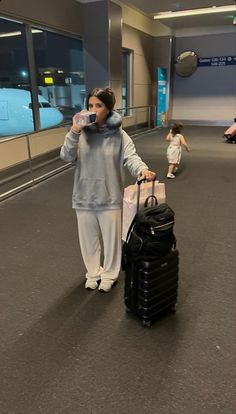 a woman is walking through an airport with her luggage and drinking from a cup in hand