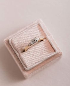 an engagement ring in a box on top of a pink cloth covered cushioned surface