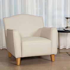 a white chair sitting in front of a window next to a table with a clock on it