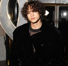 a young man with curly hair standing in front of a sign that says dv