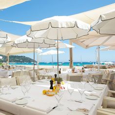 an outdoor dining area with white tables and umbrellas over the water's edge