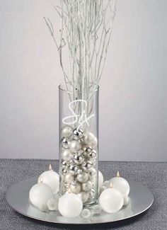 a glass vase filled with ornaments on top of a silver plate and surrounded by white balls