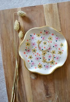 a white plate with flowers and two wedding rings on it next to dried flower stems