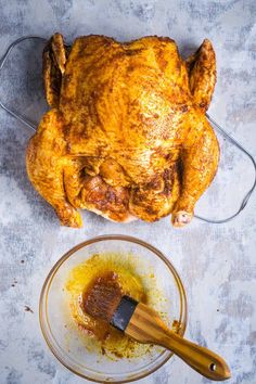 a whole chicken sitting on top of a table next to a glass bowl with mustard