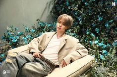 a young man sitting on top of a white couch next to blue and green flowers