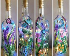 three glass bottles with flowers and butterflies in them, one has a light inside the bottle