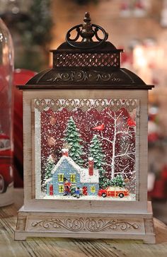 a christmas scene is displayed in a glass box on a table next to a bottle