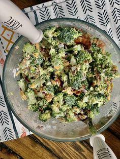 a glass bowl filled with broccoli sitting on top of a table next to a spoon