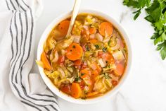 a white bowl filled with vegetable soup and garnished with parsley on the side