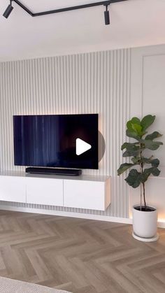 a flat screen tv sitting on top of a white entertainment center next to a potted plant