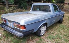 an old blue pickup truck parked on the grass in front of a fenced yard