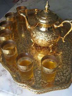 a tray topped with glasses and a tea pot filled with liquid on top of a marble table