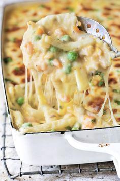 a spoon full of pasta and peas being lifted from a casserole dish on a wire rack