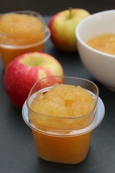 apples and oranges are sitting on a table next to cups with liquid in them