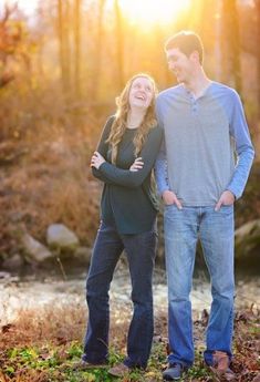 a man and woman standing next to each other in front of a river at sunset