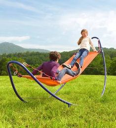 two people sitting in a hammock on the grass