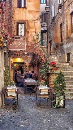 two people sitting at an outdoor table in the middle of a cobblestone street