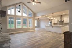 an empty kitchen and living room in a new home with large windows, wood flooring and ceiling fan