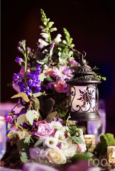 a table topped with a vase filled with purple and white flowers next to a lit candle