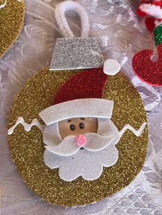 some ornaments are on a table with white and gold sequined material, including a santa clause ornament