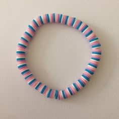 a pink, blue and green striped bracelet on a white surface with a black bead