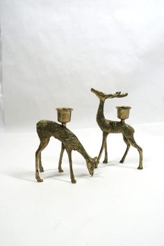 two brass deer figurines with cups on their heads, one is bending over the other