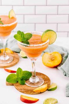 two glasses filled with fruit and garnish on top of a cutting board