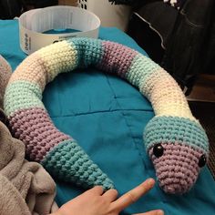 a hand pointing at a crocheted snake wreath on a blue blanket with other items in the background