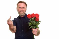 a man is holding flowers and giving the peace sign with his hand while standing against a white background